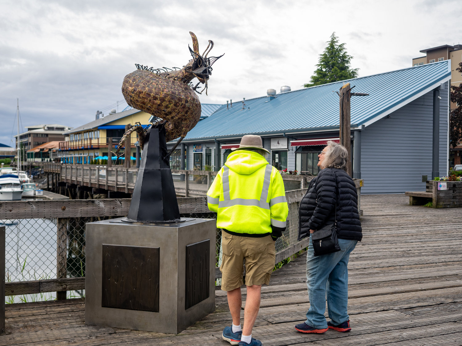 An older couple enjoying looking at the sculpture Guardian by Jim Johnson. Medium steel and copper. Percival Plinth Project sculptures on Percival Landing.